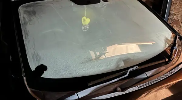 En frostig vindruta på en bil. En gul hjärtformad doftgran hänger från backspegeln.