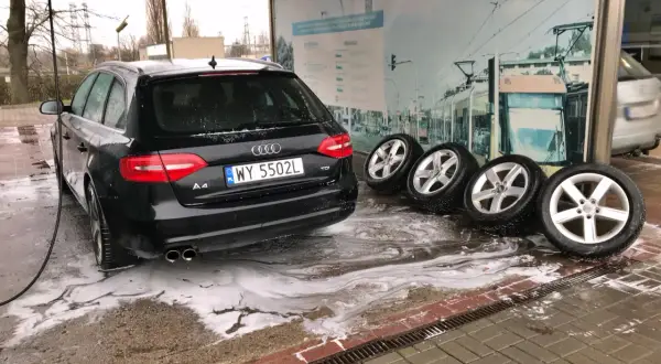 Czarny Audi na myjni bezdotykowej, obok cztery koła. Poznaj myjnia bezdotykowa triki, by Twój samochód lśnił!