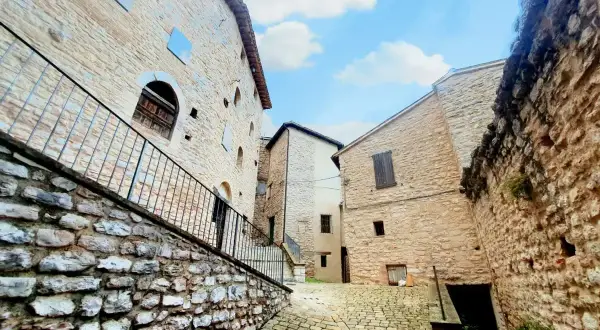 Antica via acciottolata a Caldarola, Marche, con edifici in pietra e cielo azzurro.