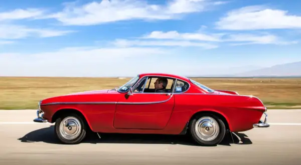 Irv Gordon kör sin röda Volvo P1800 över ett öppet fält under en klarblå himmel.