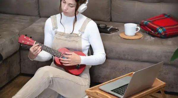 Dziewczyna w słuchawkach uczy się grać na ukulele, zastanawiając się, ile trwa nauka gry na gitarze.