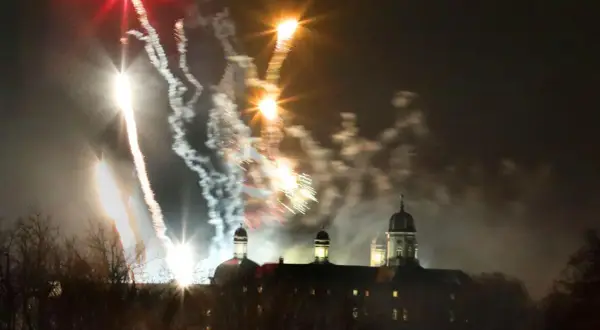 Feuerwerk über Bergisch Gladbach. Farbenfrohe Raketen erleuchten den Nachthimmel über einem historischen Gebäude mit Kuppeln.