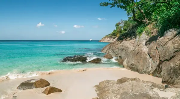 Piękne plaże Phuket z turkusową wodą, piaszczystym brzegiem i skalistym wybrzeżem. Na horyzoncie biała łódź.