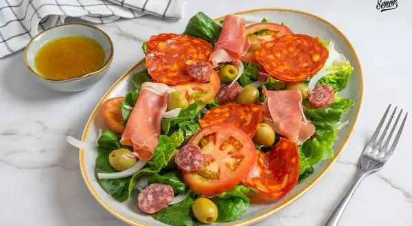 Una fresca ensalada catalana con lechuga, tomate, aceitunas, chorizo, salchichón y jamón serrano.