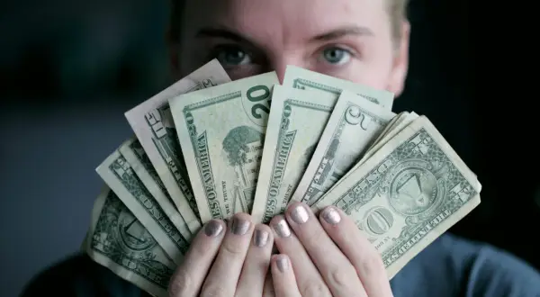 Osoba trzyma wachlarz banknotów dolarowych, zastanawiając się, czy paypal czy jest bezpieczny.