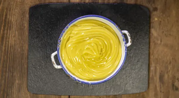 Una ciotola di cremosa crema pasticcera vegana, con un vortice lucido al centro, pronta per farcire dolci.