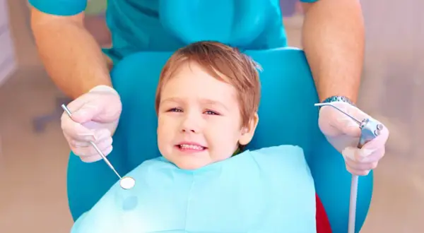 Mały pacjent u dentysty, który bada ząbki. Warto wiedzieć, co na ból zęba u dziecka, by szybko ulżyć maluchowi.