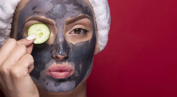 Donna con maschera viso all'argilla e fetta di cetriolo sull'occhio. La maschera viso a cosa serve? A purificare e rinfrescare la pelle.