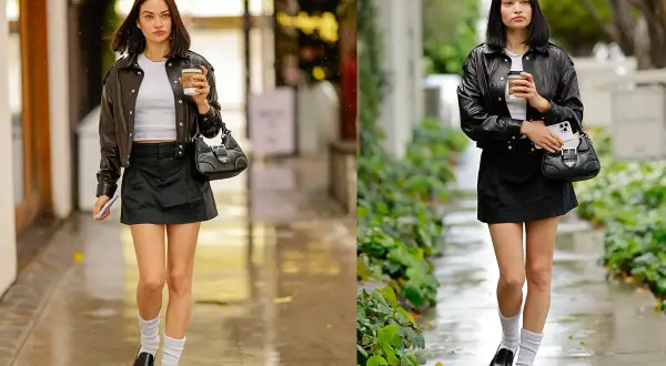 Moda urbana con giacca di pelle, minigonna nera, mocassini e calzini bianchi. La ragazza cammina con un caffè in mano.