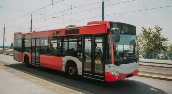 Czerwony autobus miejski jedzie po moście, w tle widać drzewa i błękitną poręcz. To idealny środek transportu, by dojechać nad morze.