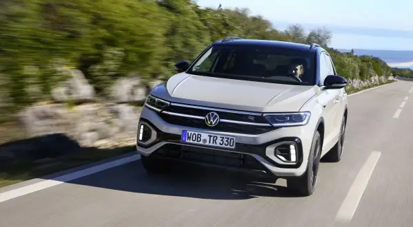 Jasnoszary Volkswagen T-Roc jedzie po krętej drodze. Nawet przy potencjalnych volkswagen t-roc usterki, auto prezentuje się dynamicznie.