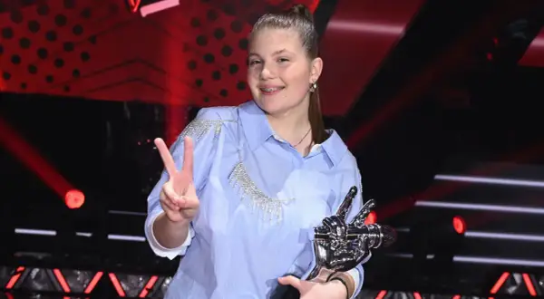 Dziewczynka w błękitnej koszuli z kryształkami, trzymająca statuetkę i pokazująca znak V.