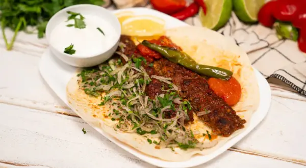 Domowy kebab z mięsem, cebulą, pietruszką, pomidorami i sosem jogurtowym na placku.