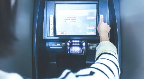 Ręka naciska przycisk na bankomacie. Ekran pokazuje opcje: "Deposit", "Withdrawal", "Main Menu". Czy z konta dziecka można robić przelewy?
