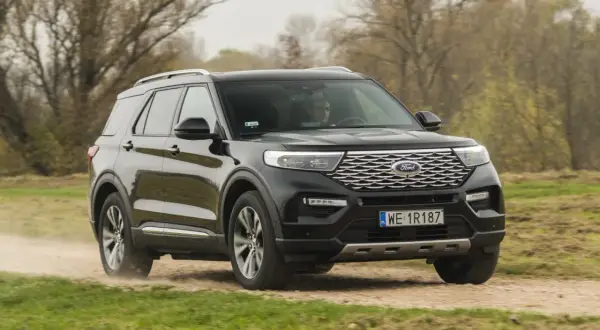 Czarny Ford Explorer 4x4 pokonuje piaszczystą drogę wśród drzew.
