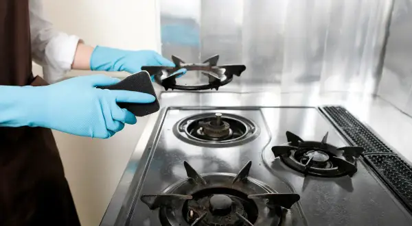 Mani con guanti azzurri puliscono fornelli a gas con una spugna. Guida su come pulire i fornelli del gas per una cucina splendente.