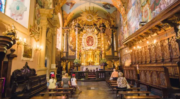 Wnętrze sanktuarium pasyjno-maryjnego w Kalwarii Zebrzydowskiej. Złoty ołtarz, malowidła na ścianach i sklepieniu, wierni na ławkach.