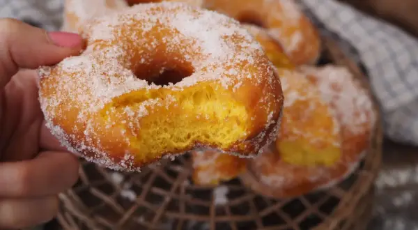 En hand håller en sockerdränkt munk, perfekt för ett hembakat donuts recept.