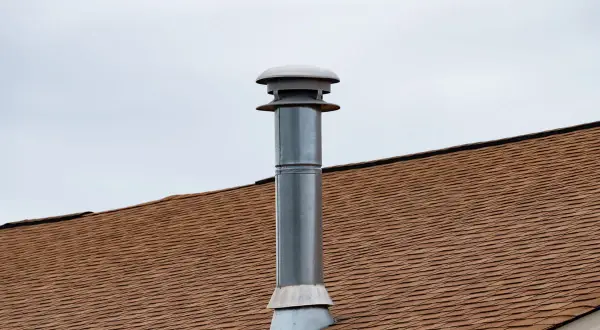 Cheminée sans tubage sur un toit brun sous un ciel couvert. La cheminée est en métal avec un chapeau ventilé.