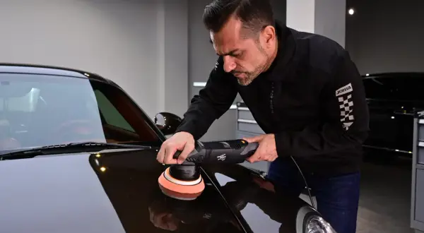 Man polerar en mörk bil med en polermaskin. En demonstration av hur polerar man en bil för att få en spegelblank yta.