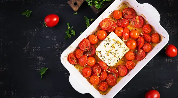Tomates cerises au four, tendres et juteuses, baignant dans leur jus avec un bloc de feta crémeuse. Un délice simple et savoureux.