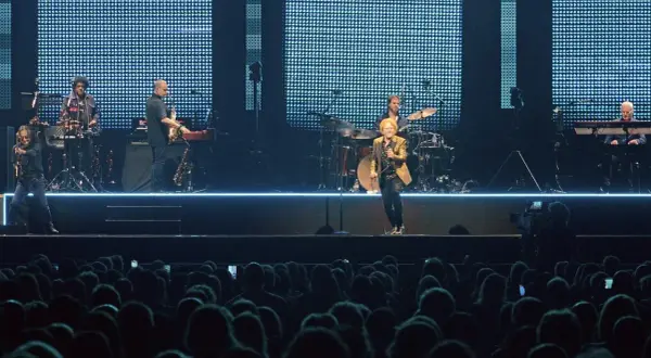 Ein Musiker mit goldenem Sakko singt auf der Bühne, umgeben von seiner Band. Ein Konzert von Simply Red in Stuttgart.