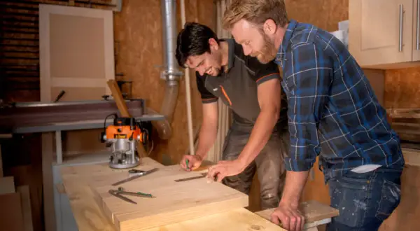 Carpinteros trabajan con madera calabo en un taller. Uno marca una pieza de madera mientras el otro observa.