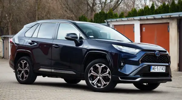 Ciemnoniebieski Toyota RAV4 Hybrid, często chwalony w toyota rav4 opinie, zaparkowany przed garażami.