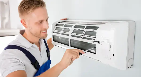 Un technicien ajuste un climatiseur mural. Il s'assure que l'appareil fonctionne bien pour éviter toute mauvaise odeur de climatisation.