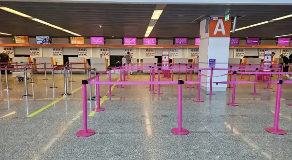 Puste stanowiska odprawy na lotnisku, z różowymi barierkami i tablicami Wizz Air.
