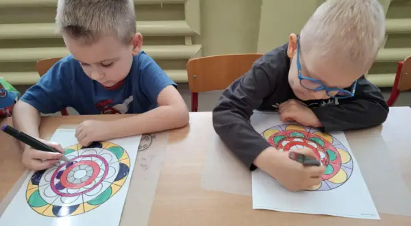 Dwóch chłopców z zapałem koloruje swoje mandale.
