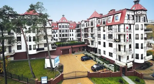 Elegancki budynek w stylu alpejskim, przypominający Continental Hotel Krynica, z białymi fasadami, czerwonymi dachami i drewnianymi elementami.