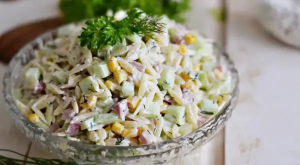 Pyszna sałatka z makaronem orzo, ogórkiem, kukurydzą i szynką, udekorowana natką pietruszki i koperkiem.