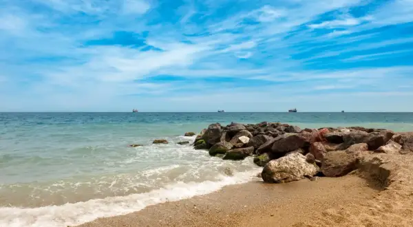 Olas rompiendo en la arena dorada de la playa Quitapellejos. El mar turquesa se extiende hasta el horizonte, con barcos navegando. ¡Un lugar ideal para relajarse!