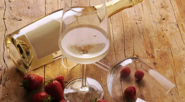 Butelka i kieliszek pełne musującego płynu, obok truskawki i maliny. To jest prosecco, idealne na letnie popołudnie.