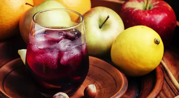 Un refrescante tinto de verano con espuma de limón, rodeado de frutas frescas como naranjas, manzanas y un limón amarillo.
