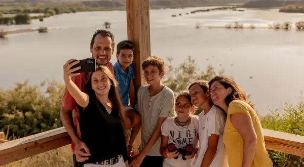 Familia sonriente se toma un selfie con un lago de fondo. Un día perfecto en la playa de Vera para niños, explorando la naturaleza.