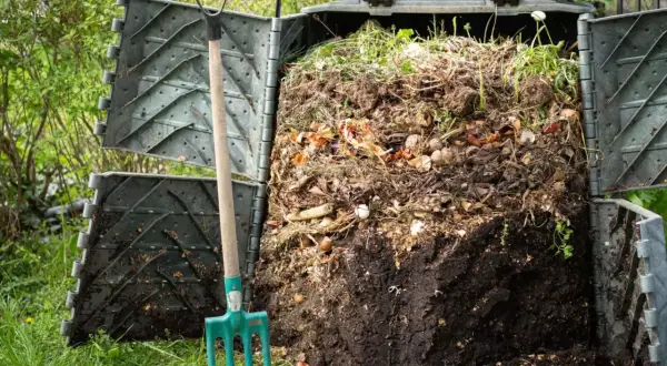 Kompostownik z plastiku, pełen resztek organicznych, obok widły. Idealne miejsce, by dowiedzieć się, z czego zrobić kompostownik.