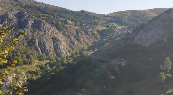 Malowniczy widok na dolinę z krętą drogą, domkami na zboczu i skalistymi górami. W oddali majaczy szczyt Naranjo de Bulnes.