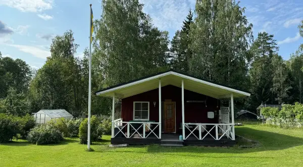 Rött hus med veranda och flaggstång i Stjärnsund. En växthus syns i bakgrunden.