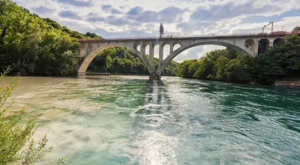 Ponte ad arco su fiume con acque di colori diversi, dove si intravedono segnali navigazione fluviale.