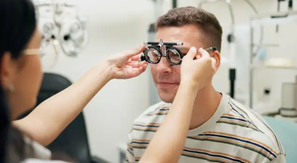 Okulista dopasowuje soczewki próbne mężczyźnie. Idealny moment, by skorzystać z promocji na okulary i zadbać o wzrok.