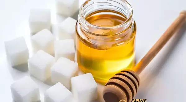 Słoik miodu, kostki cukru i drewniana chochla do miodu.