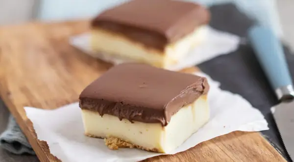 Zwei rechteckige Stücke schokokuchen mit vanillepudding, bedeckt mit Schokolade, auf einem Holzbrett.