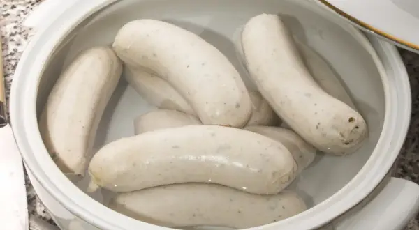Biała kiełbasa w garnku z wodą, gotowa do parzenia. Delikatne kiełbaski czekają na idealny moment.