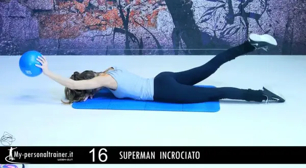 Donna esegue esercizio "Superman incrociato" per rafforzare i lombari muscoli, sollevando una gamba e un braccio con una palla blu.