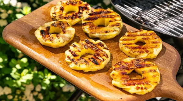 Gegrillte Ananasscheiben mit karamellisierten Rändern auf einem Holzbrett, bereit zum Servieren. Das Ananas grillen bringt süße Aromen hervor.