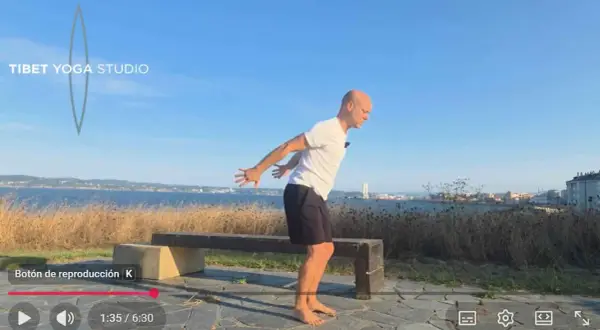Hombre practicando yoga tibetano al aire libre, con el mar y la ciudad de fondo.
