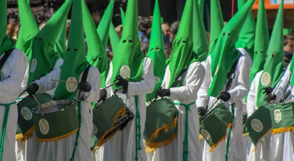 Nazarenos con túnicas blancas y capirotes verdes desfilan en la ruta cofrade Zaragoza, tambores resonando.