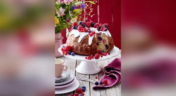 Ein köstlicher Gugelhupf mit Mandeln, Beeren und Zuckerguss, dekoriert mit frischen Früchten.